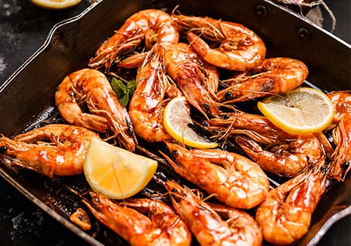 Traditional fried black tiger prawn with lemon as top view on a rustic old board.