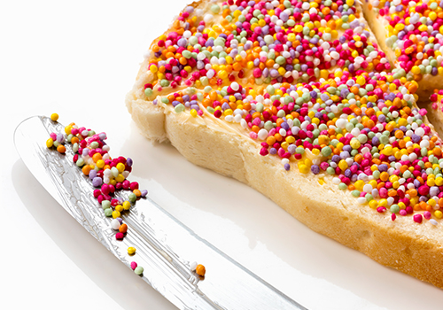 A top-down photo of fairy bread cut diagonally with a butter knife between the pieces.