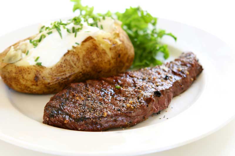 Steak with baked potato and lettuce on a white plate.
