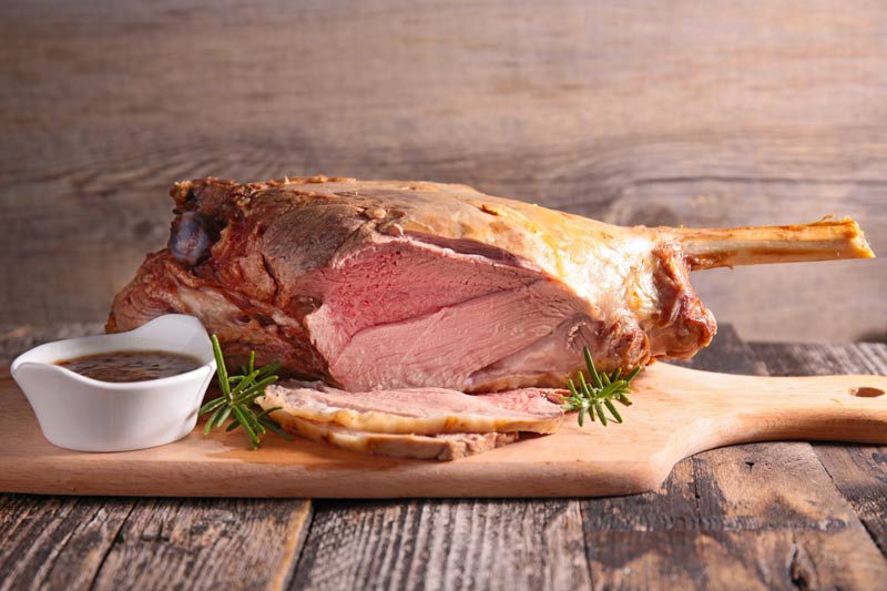 Roasted lamb leg on a wooden board with rosemary and gravy