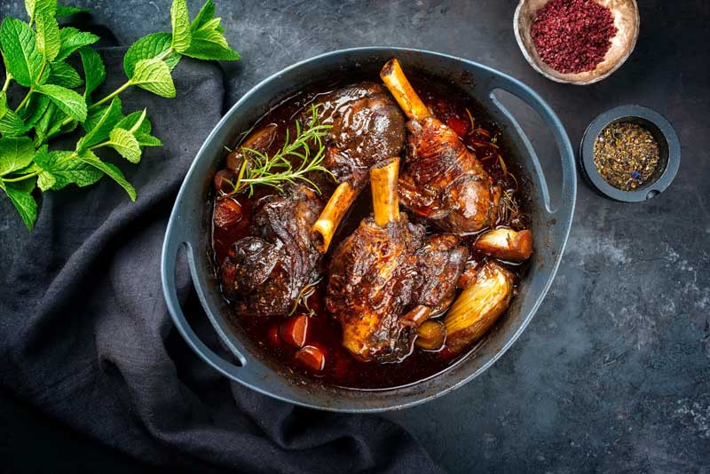 Roasted lamb shanks with rosemary in a roasting dish.