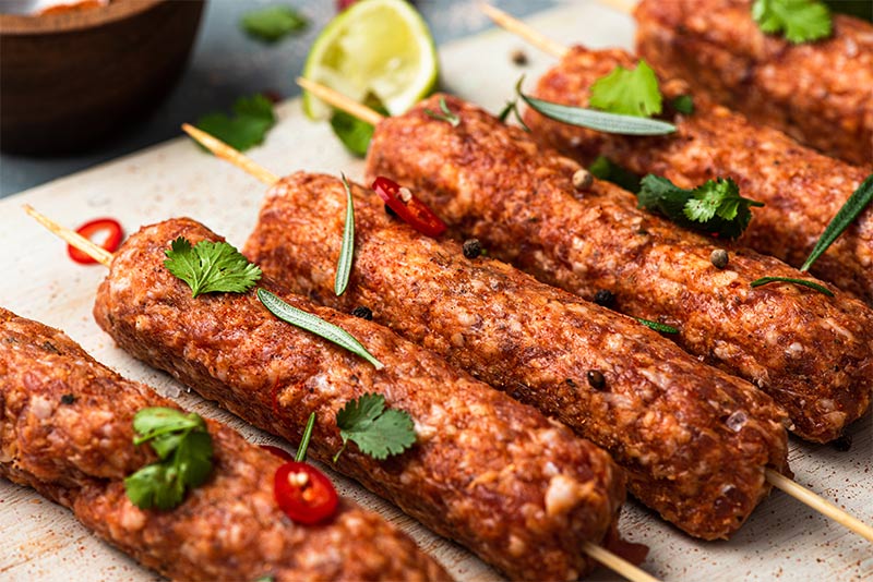 Lamb kebabs on skewers with parsley, chillies, rosemary leaves and fresh lime.