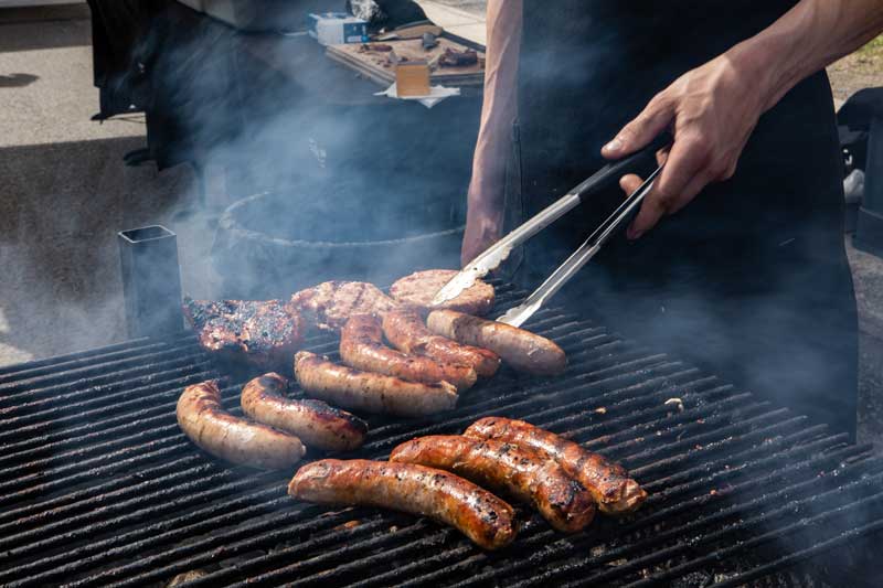 Man cooking sausages and burgers on a barbecue.