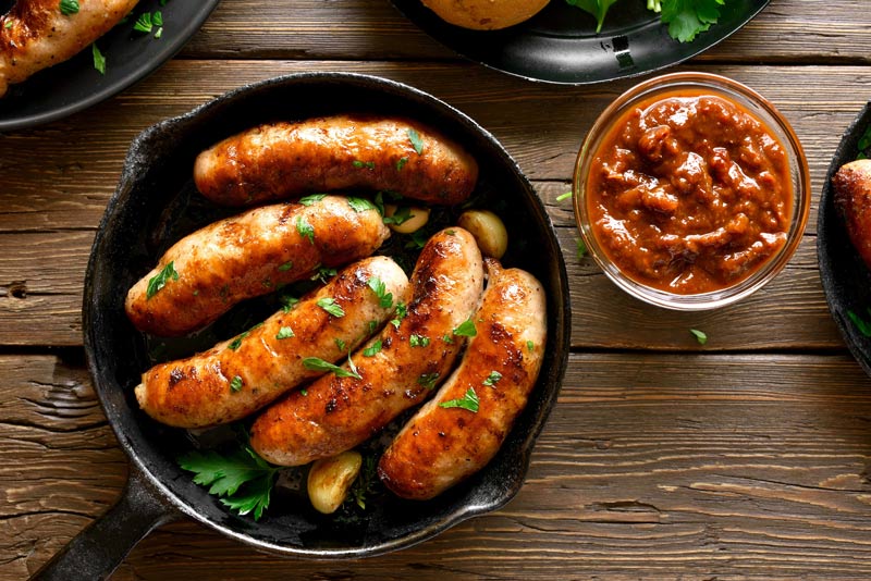 Pan-fried sausages with parsley in a cast iron pan with a dish of salsa.